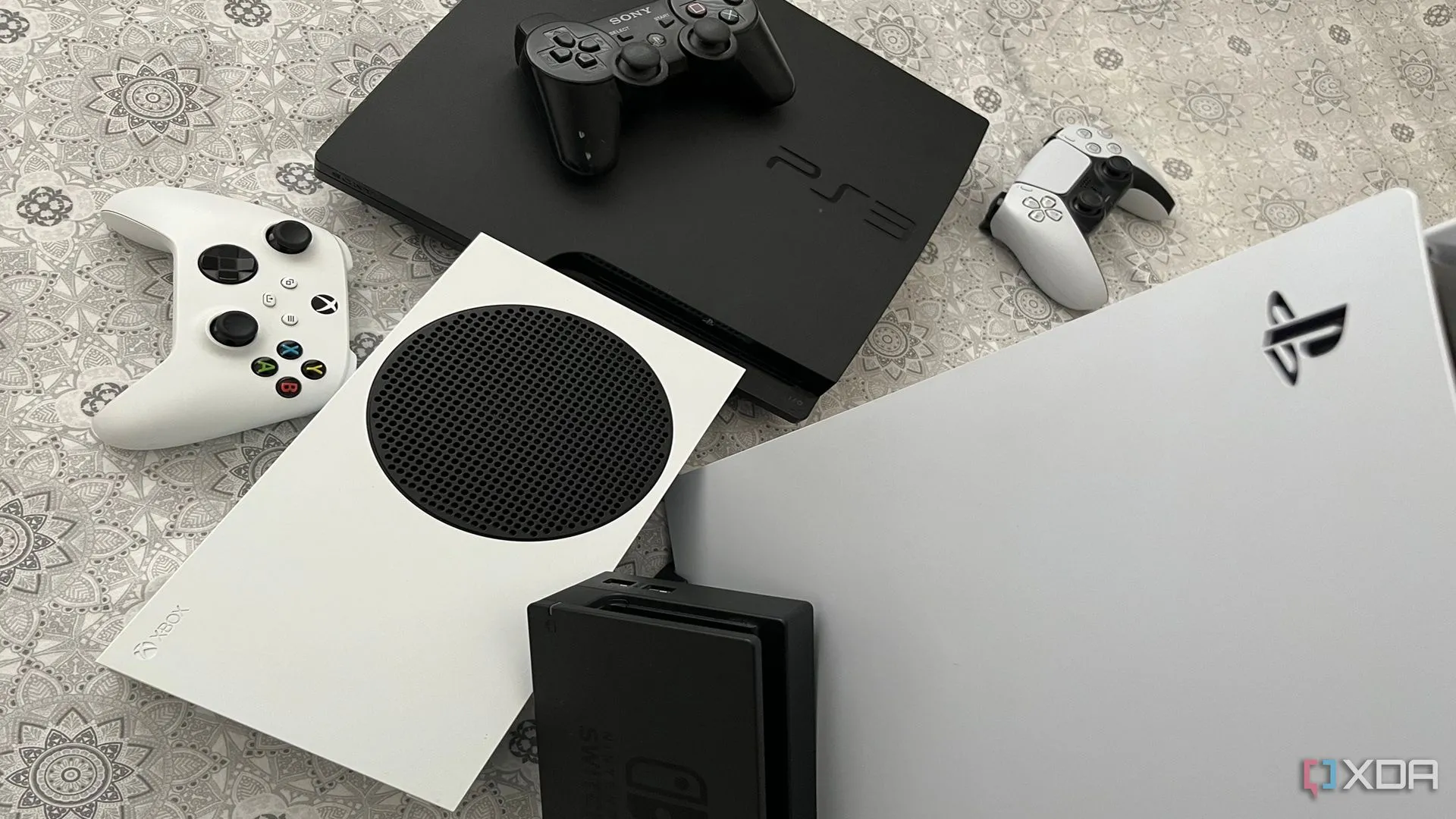 Bộ sưu tập các máy console Playstation 5, Xbox Series X, đế sạc Nintendo Switch và PlayStation 3 đặt cạnh nhau