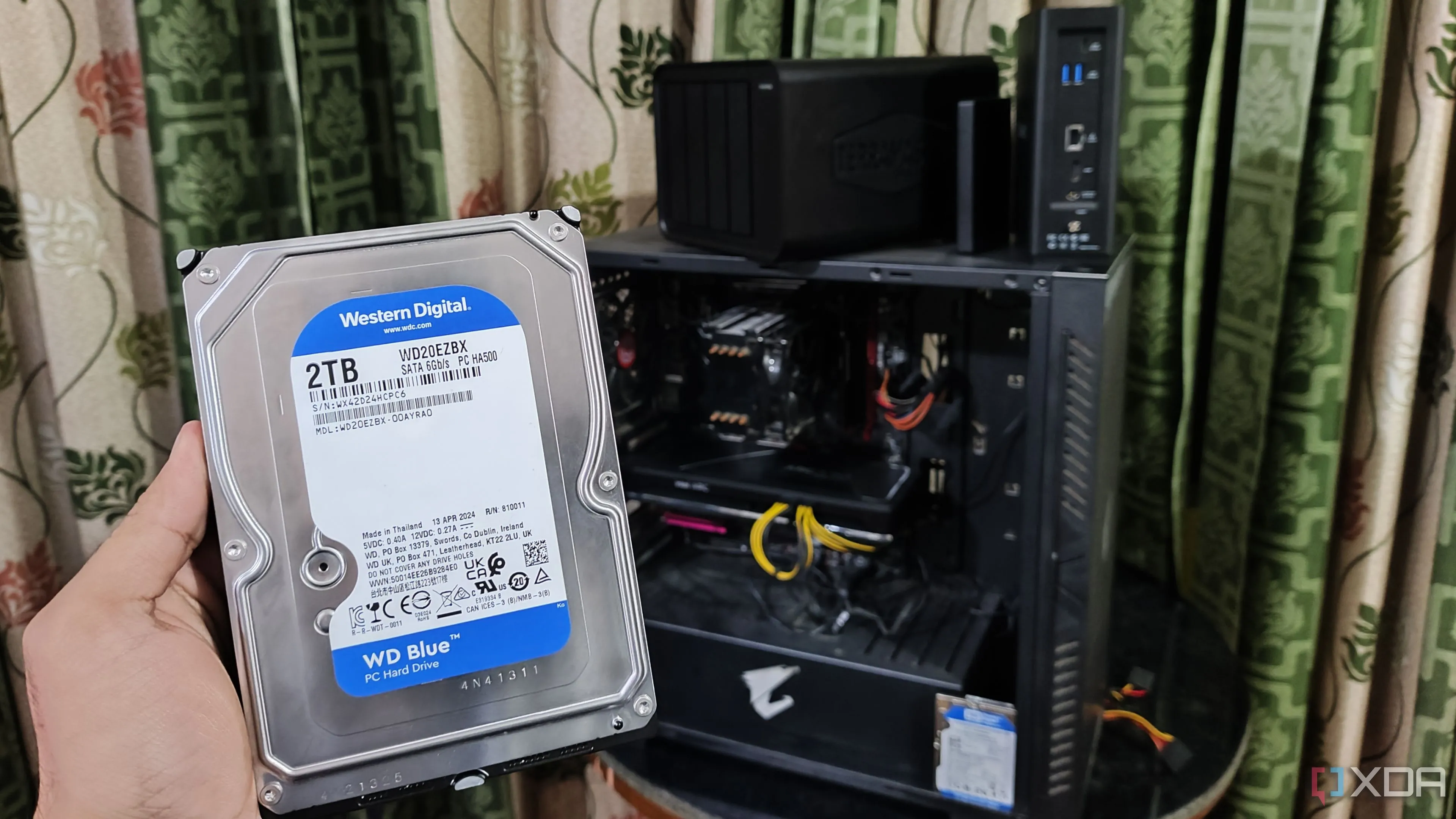 Người dùng đang cầm ổ cứng HDD trước máy tính và hai thiết bị NAS TerraMaster