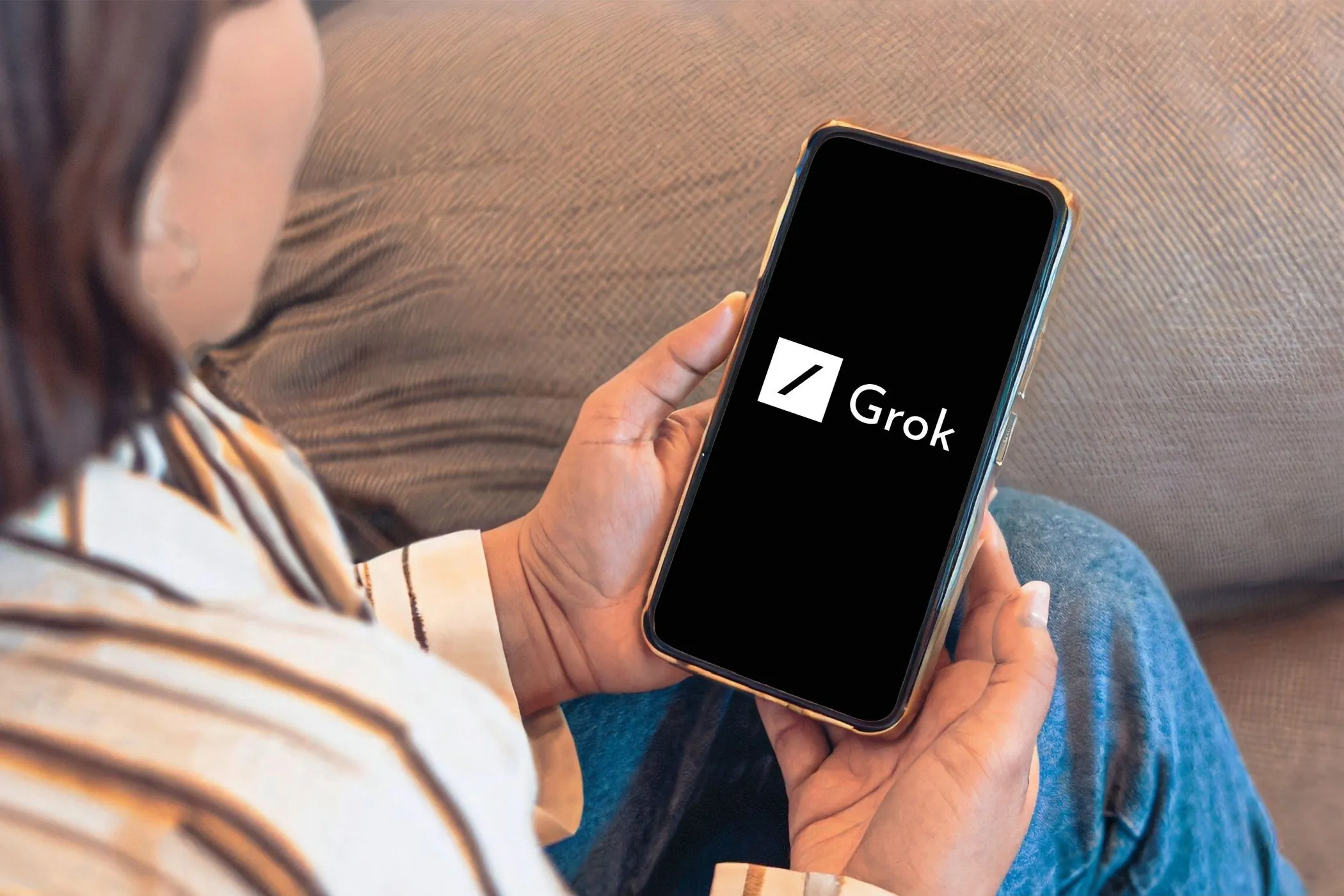 Một người đang xem điện thoại thông minh hiển thị logo Grok AI