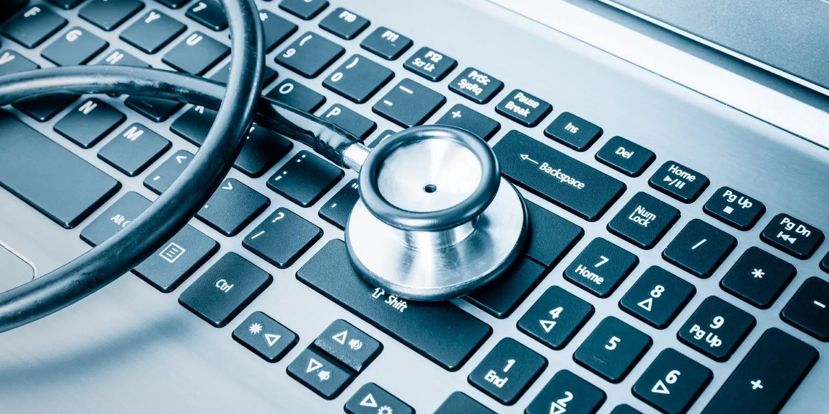 Bàn phím laptop và ống nghe y tế, tượng trưng cho việc kiểm tra và phòng ngừa rủi ro bảo mật trên các thiết bị công nghệ.