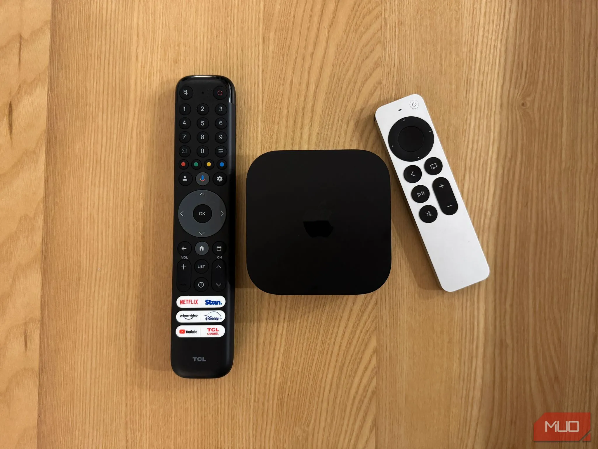 Bộ ba Apple TV, Siri Remote và điều khiển TV TCL trên mặt bàn, làm nổi bật sự khác biệt về thiết kế