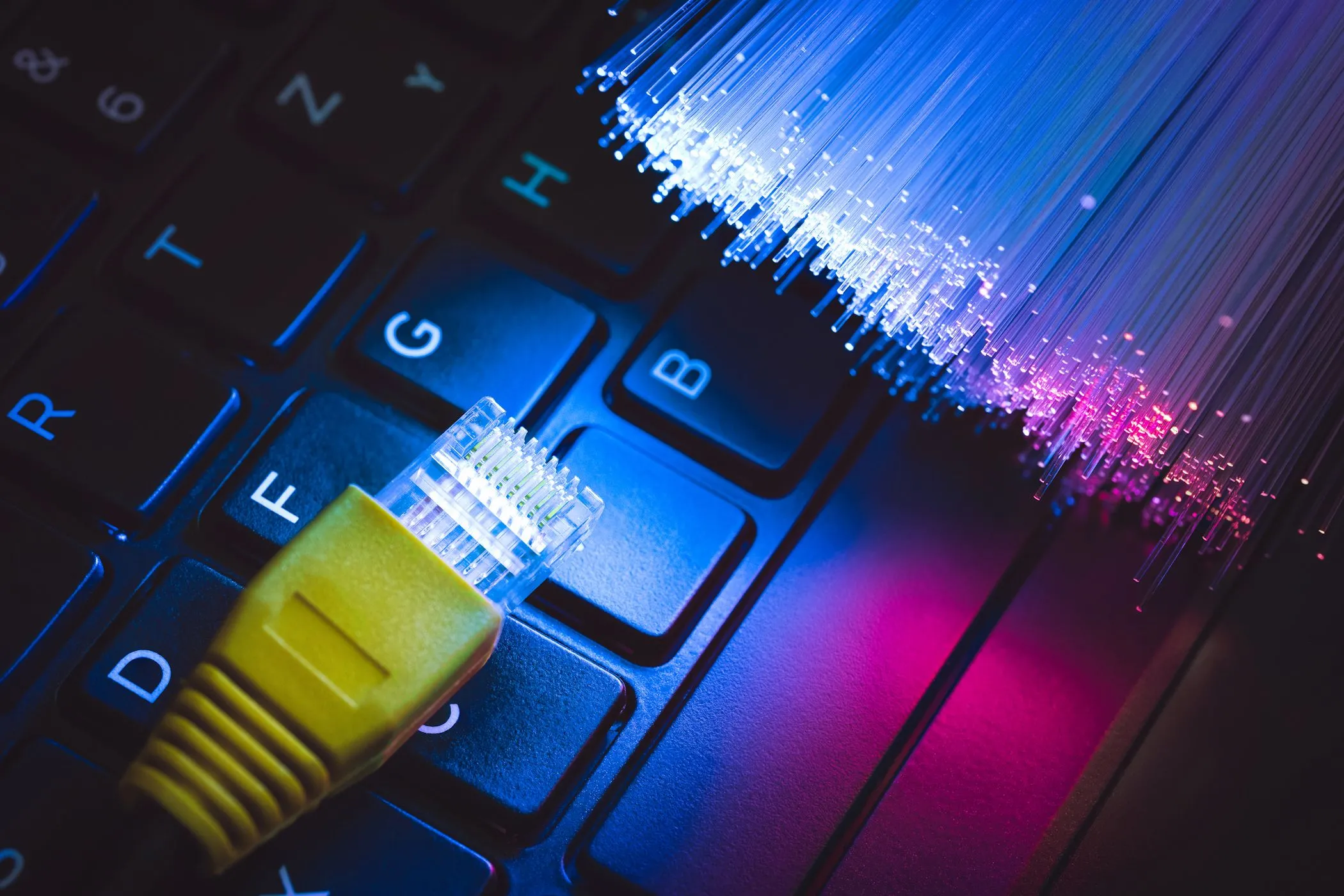 Dây cáp Ethernet kết nối với bàn phím laptop cùng cáp quang, biểu tượng cho băng thông và kết nối có dây