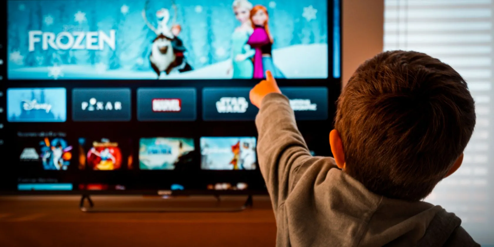 Em bé chỉ vào ứng dụng Disney+ trên màn hình TV, minh họa cách thiết lập TV cũ thành trạm giải trí an toàn cho trẻ.