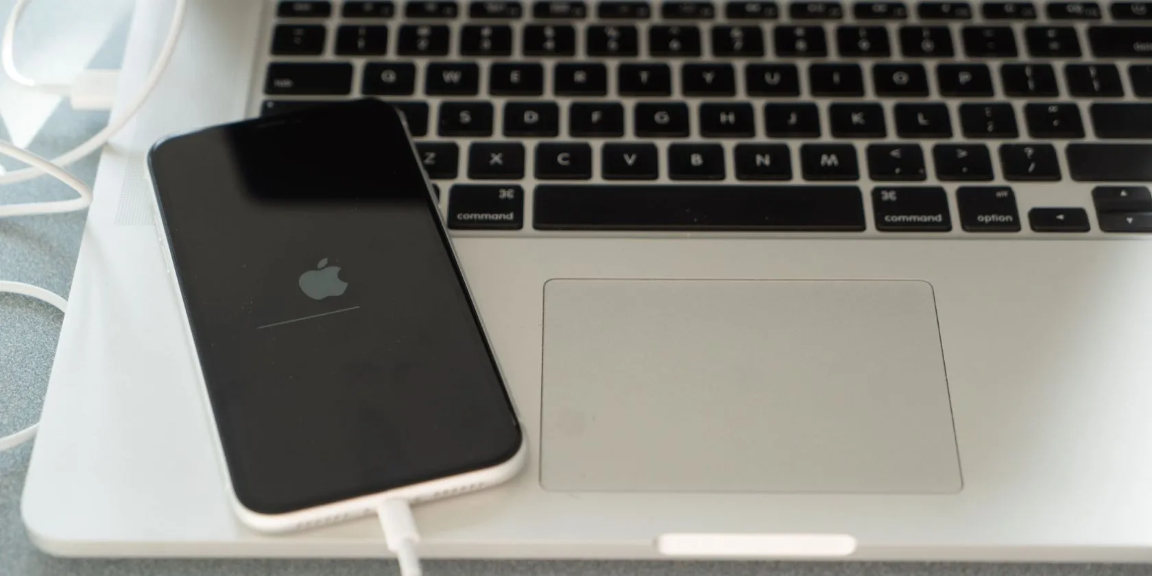 Hình ảnh một chiếc iPhone đang được kết nối với MacBook, biểu thị quá trình khôi phục cài đặt gốc hoặc reset thiết bị