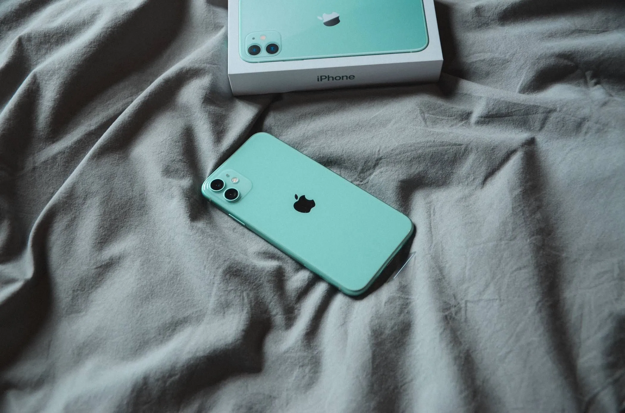 iPhone đặt trên chăn hoặc ga trải giường khi đang sạc, minh họa nguy cơ quá nhiệt khi sạc trên bề mặt kín.