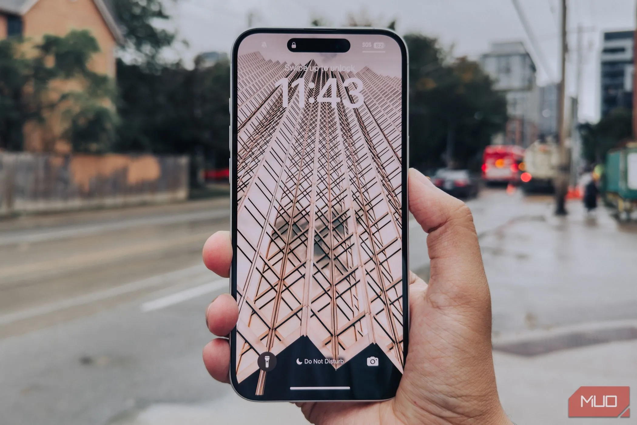 Màn hình iPhone 16 Plus với viền mỏng được cầm trên tay, hậu cảnh là thành phố