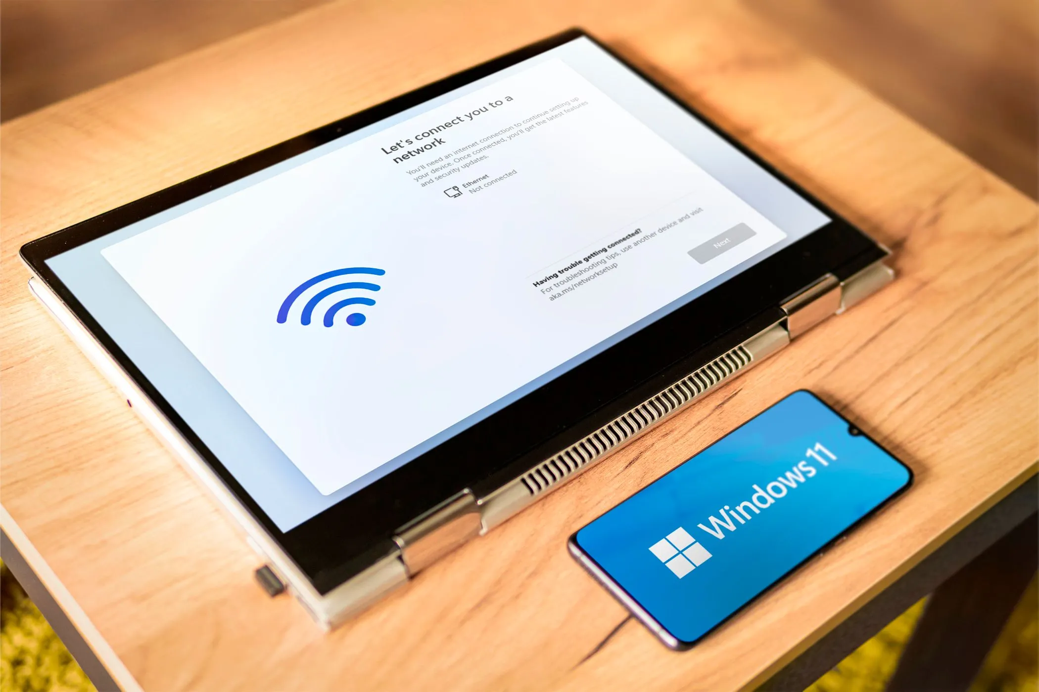 Màn hình máy tính xách tay và điện thoại Android hiển thị logo Windows 11, minh họa việc dùng điện thoại làm màn hình phụ