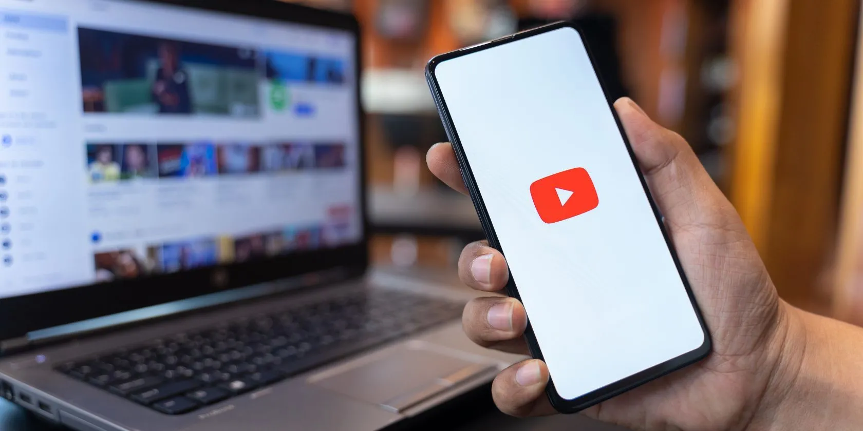 Một người cầm điện thoại hiển thị ứng dụng YouTube và trang web YouTube phía sau