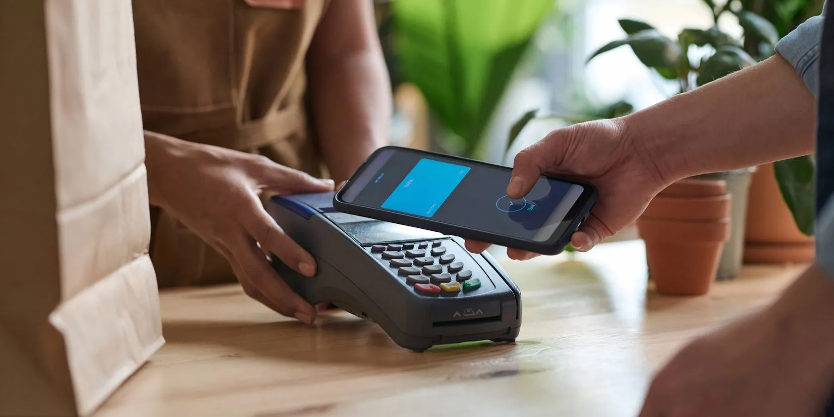 Một người đàn ông đang thanh toán không tiếp xúc bằng điện thoại thông minh qua chip NFC ở mặt lưng tại quầy hàng tạp hóa