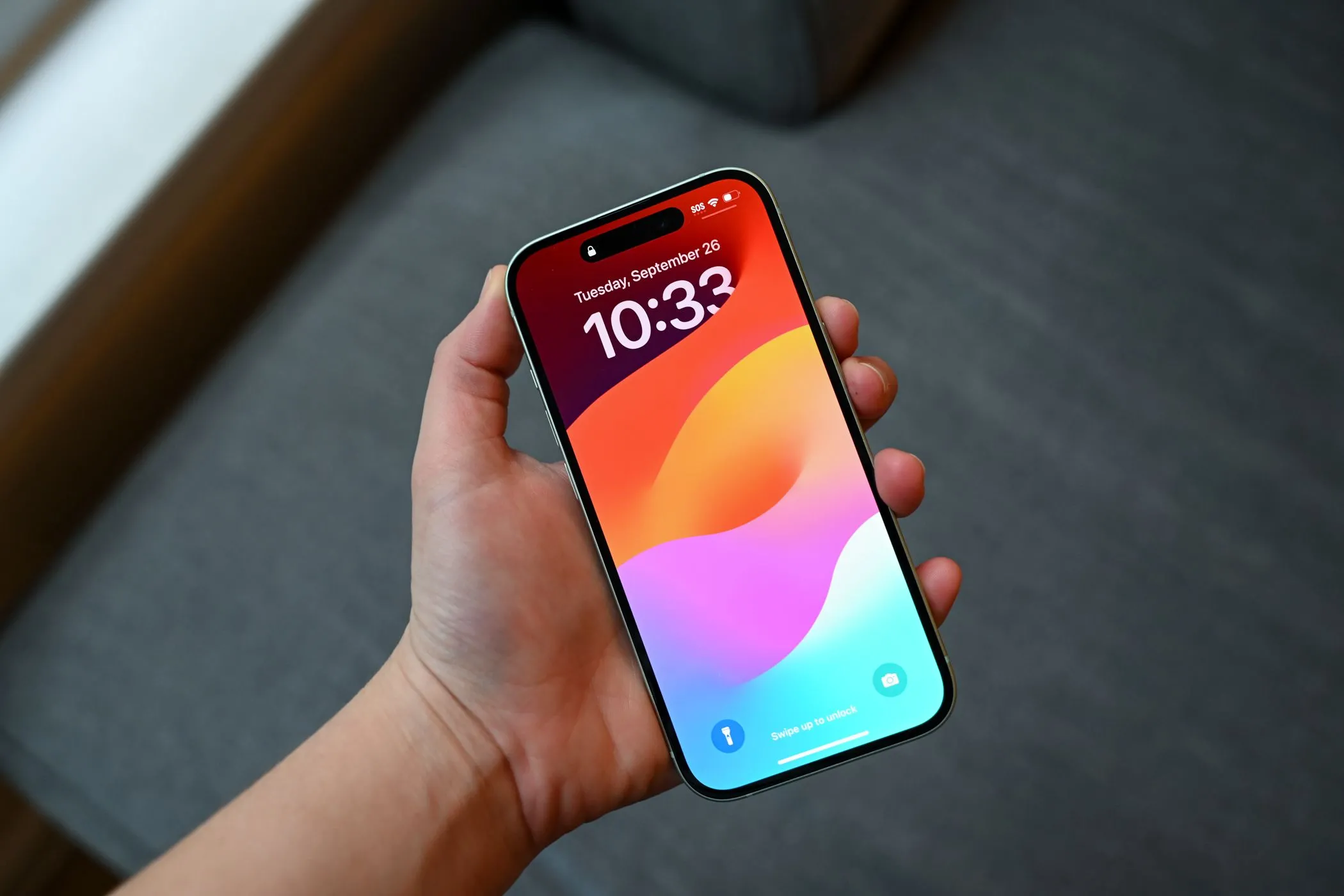 Người dùng cầm iPhone 15 đang hiển thị màn hình khóa với miếng dán bảo vệ