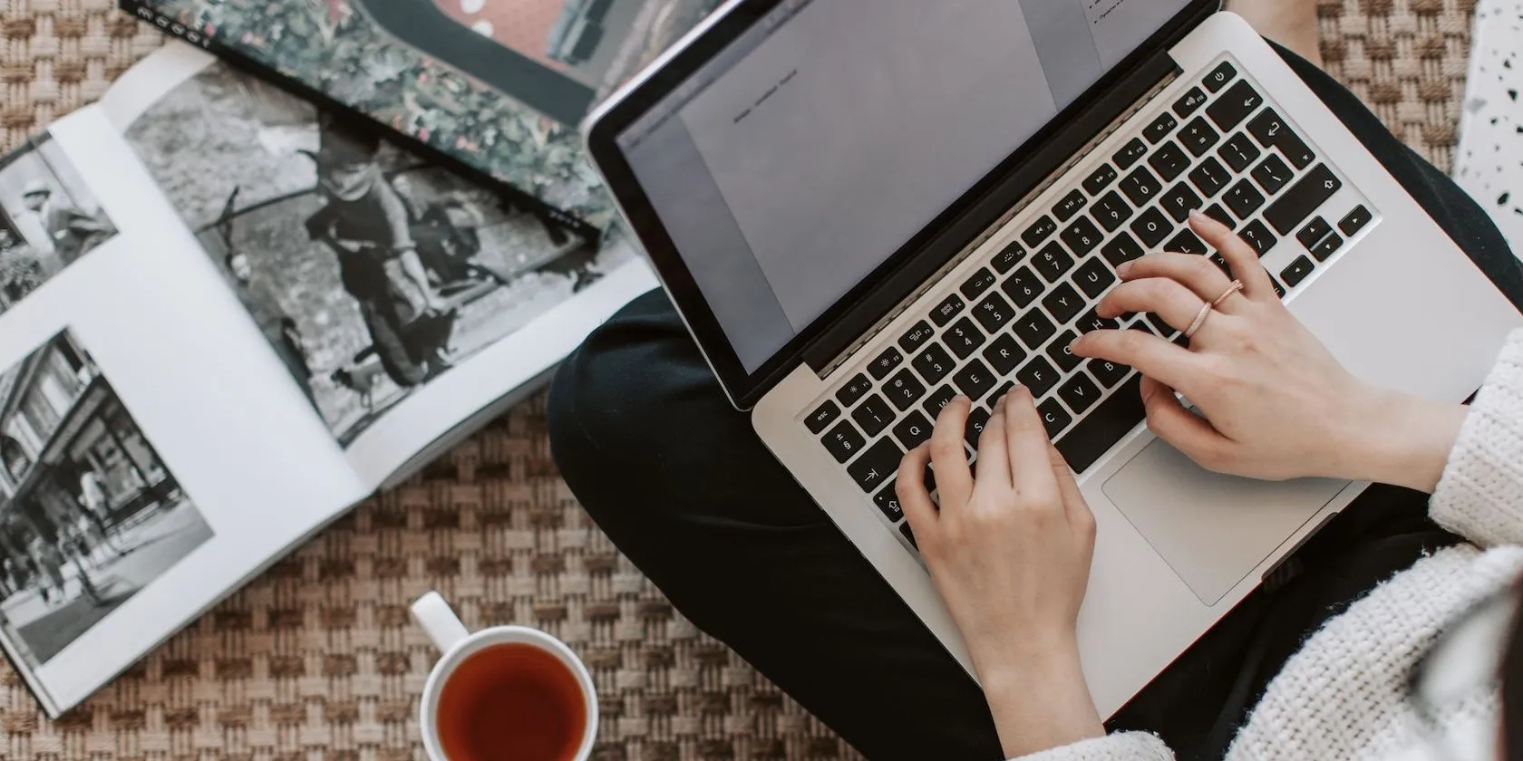 Người phụ nữ làm việc trên laptop với sách và cốc trà trên bàn