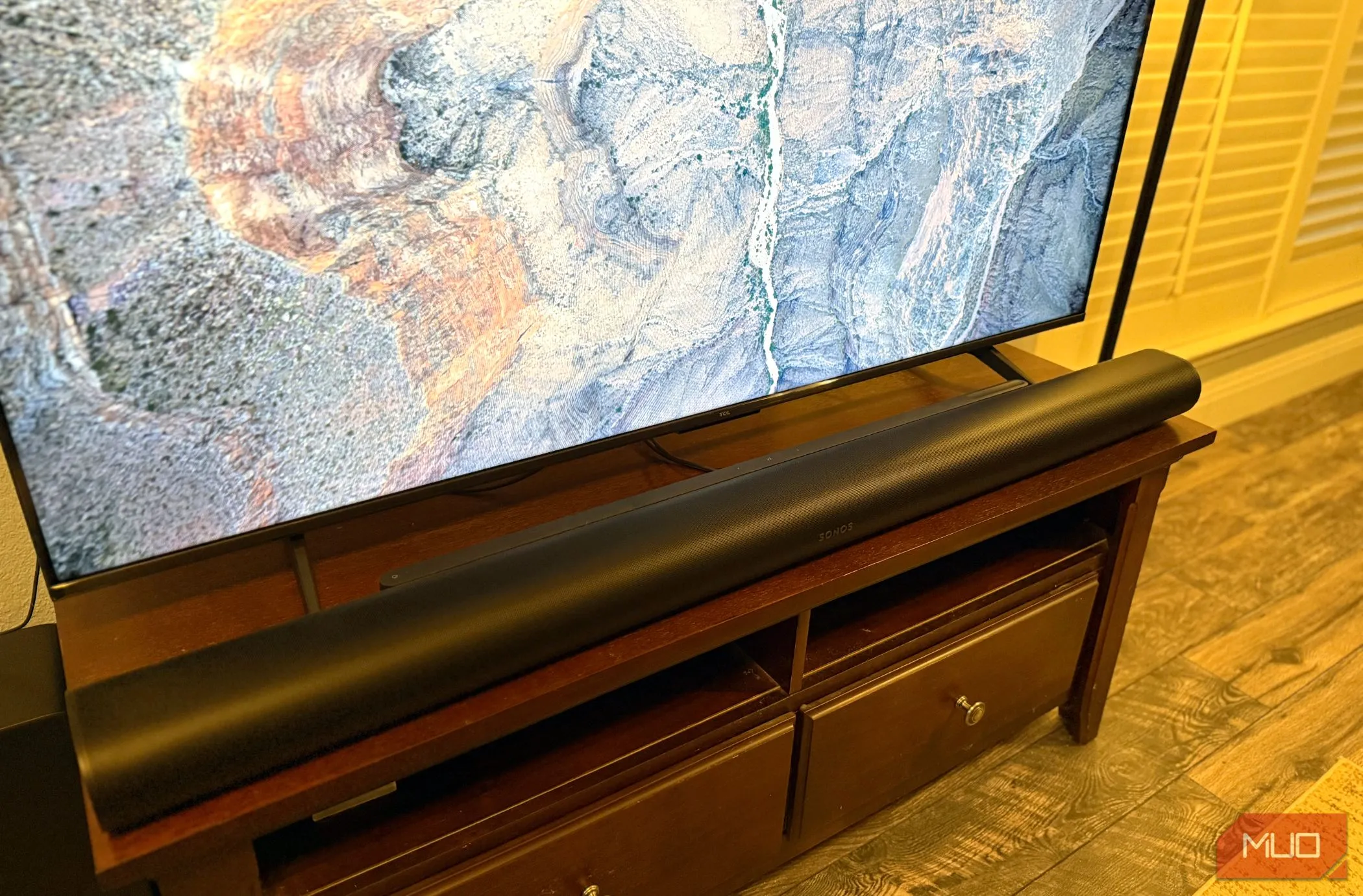 Sonos Arc Ultra màu đen nhìn từ cạnh bên, đặt trên kệ TV cạnh màn hình lớn, làm nổi bật kích thước ấn tượng của soundbar.